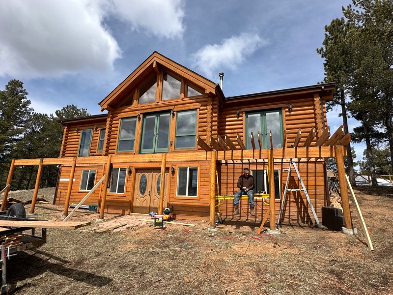 Cedar pergola and deck framing across the front of a log home