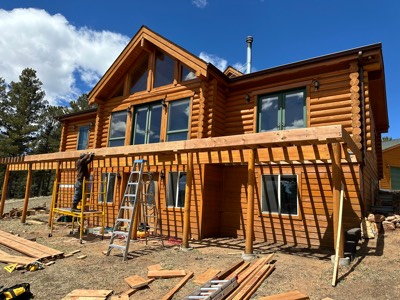 Worker on a ladder installing pergola rafters on a log home